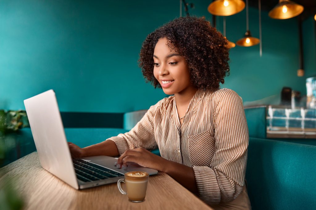 Woman looking at laptop screen in a coffee shop with blurred background and teal coloured walls