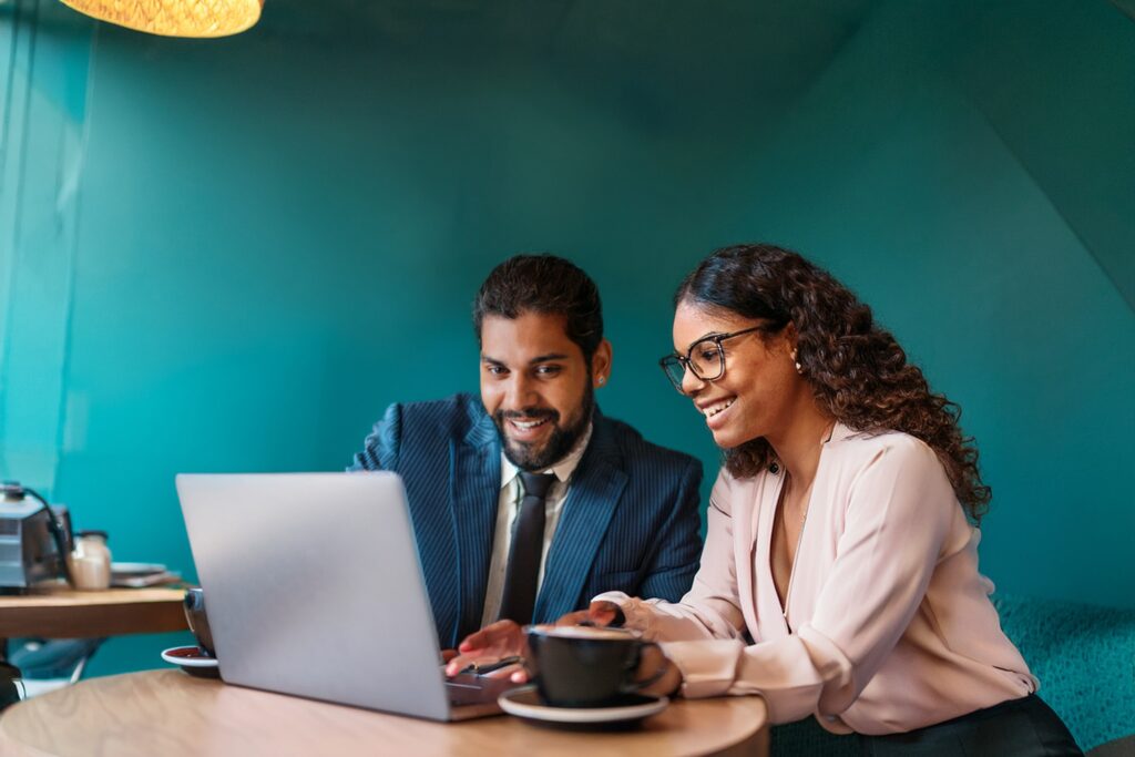 Business man in coffee shop with teal coloured walls showing a woman somwthing on his laptop