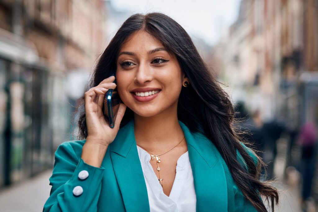 Business woman in teal coloured jacket speaking on the phone in an English street